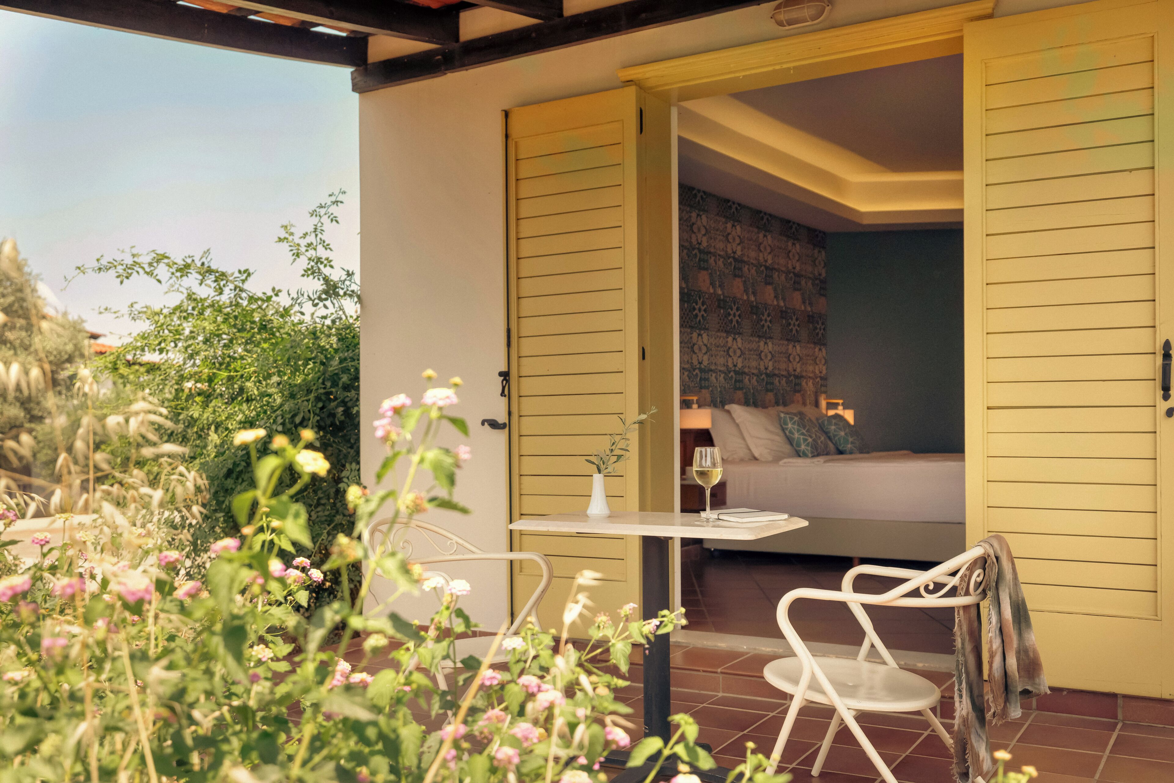 Un patio abierto con una mesa y sillas de comedor, una cama con almohadas, y vistas al jardín.