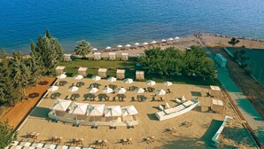 An aerial view of a beach with rows of beach umbrellas and lounge chairs, a sandy beach area, and a pathway leading to the beach. - Zeus Eretria Resort  (Eretria)