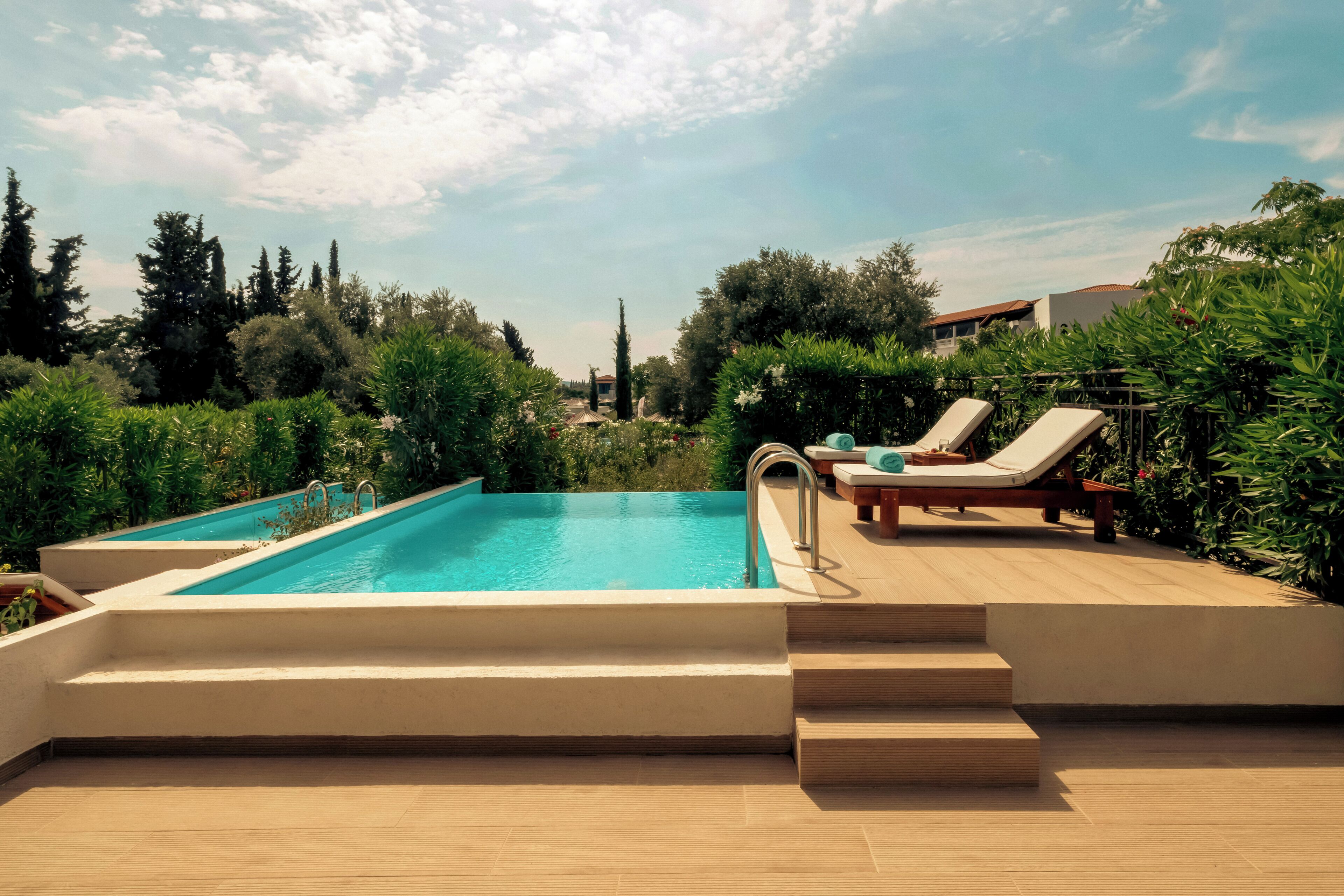 A swimming pool with steps leading down to the water, surrounded by greenery and a clear sky.