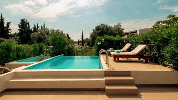 A swimming pool with steps leading down to the water, surrounded by greenery and a clear sky.
