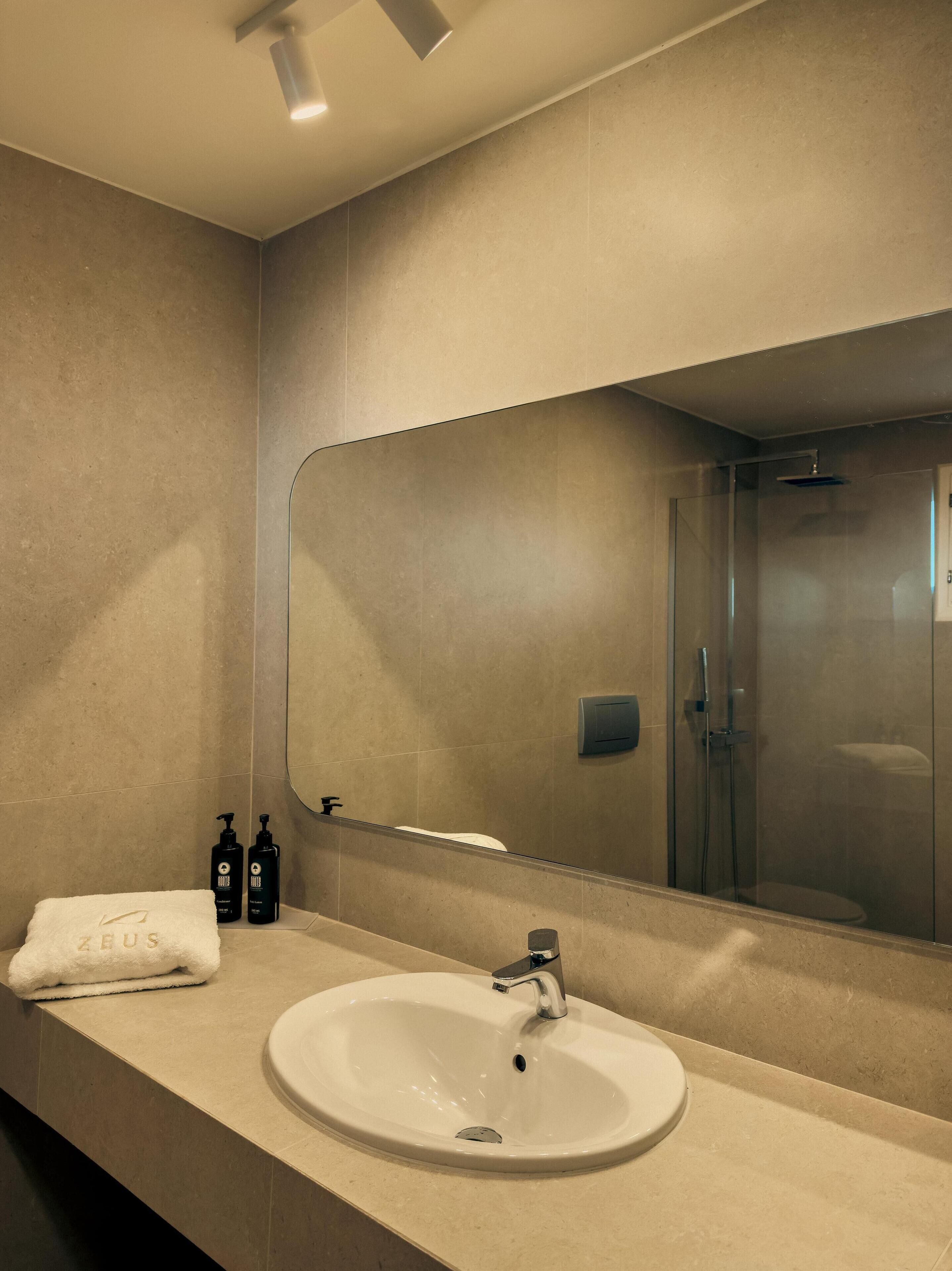 Een badkamer met een wit wastafelmeubel, een grote spiegel en een douchecabine van glas.