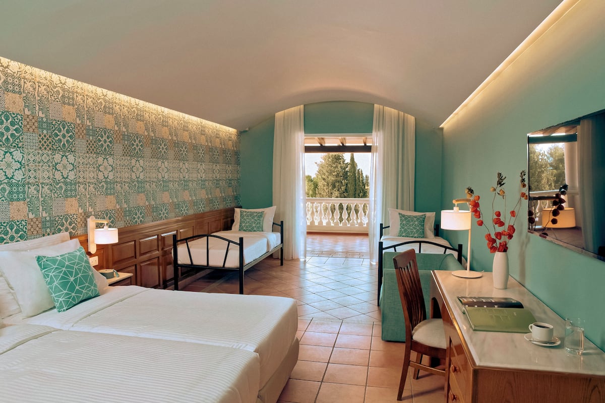 Een hotelkamer met een groot bed, twee nachtkastjes, een bureau met stoel, een raam met uitzicht op de omgeving, en een decoratieve spiegel.