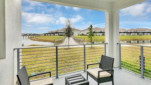 Ein Balkon mit zwei Korbstühlen und einem kleinen Tisch, der auf eine Grünfläche mit einem Weg und Gebäuden im Hintergrund blickt.