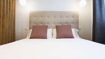 A neatly made bed with a tufted headboard, two pillows, and two pendant lights.