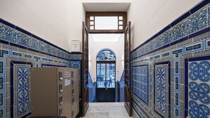 Un pasillo con baldosas azules y blancas con estampado, una puerta de madera y un suelo de mármol.