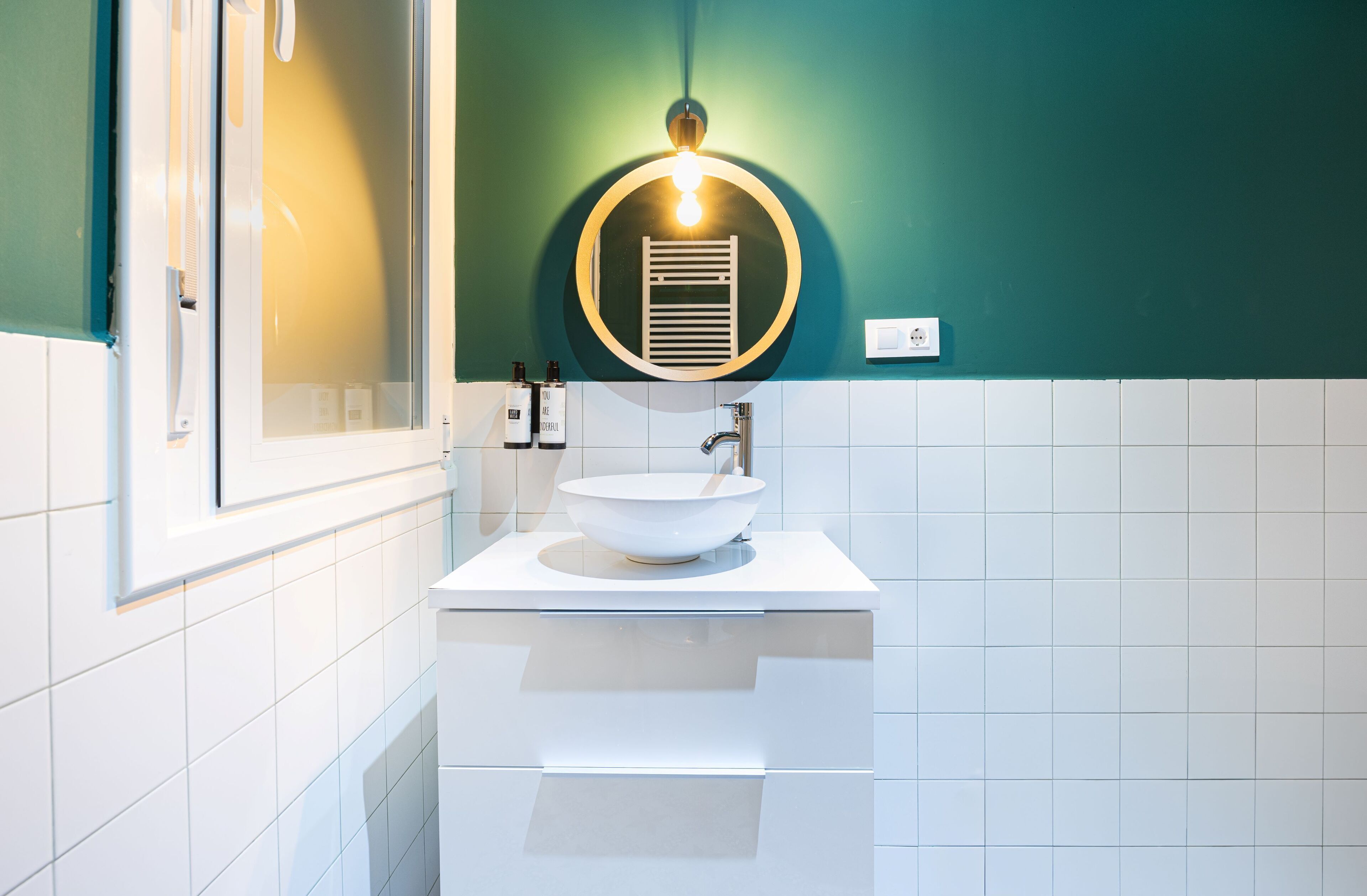 Un baño moderno con un lavabo blanco, un espejo y un aplique de pared.
