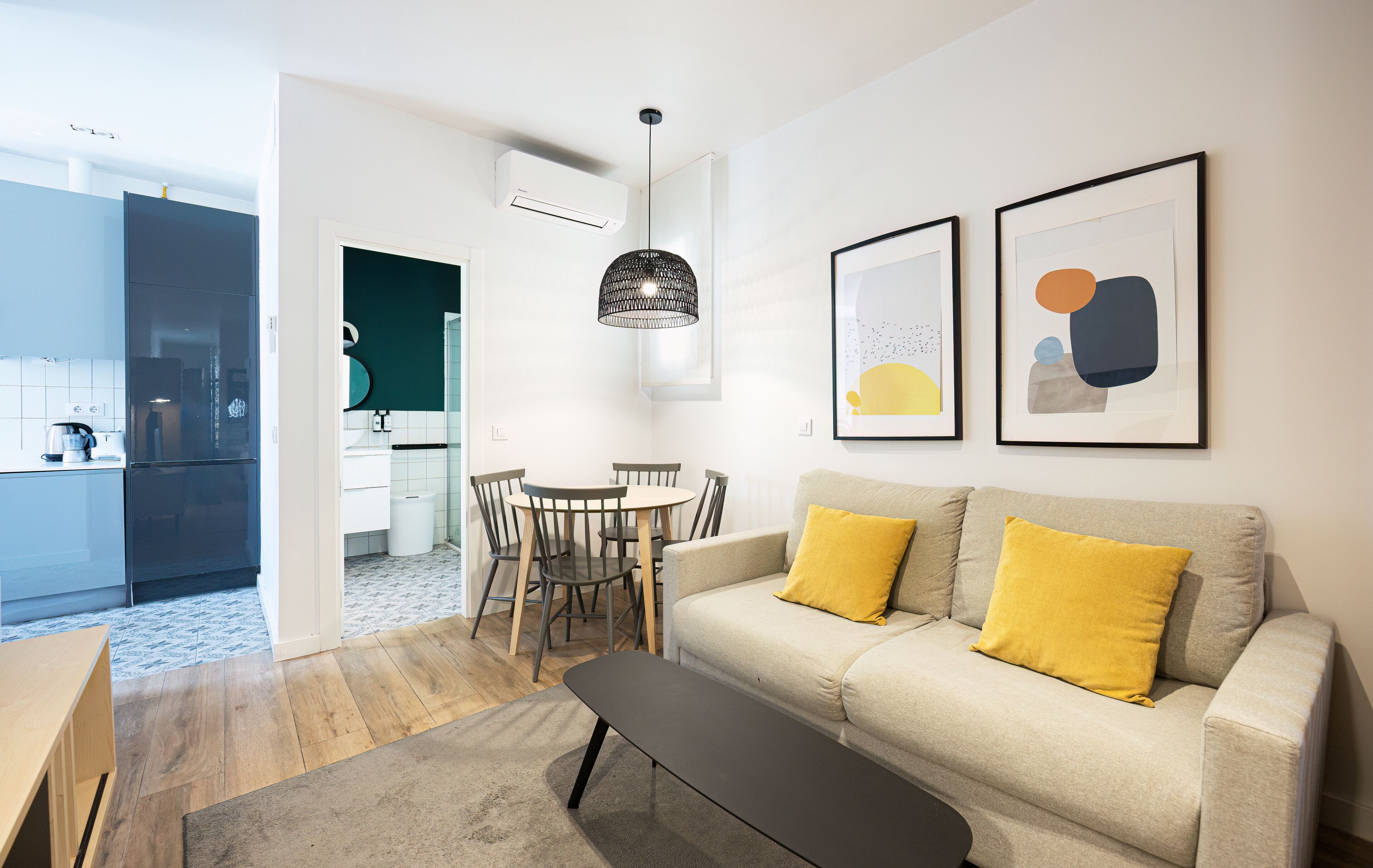Una sala de estar moderna con un sofá, una mesa de comedor y sillas. Se ve una cocina al fondo.