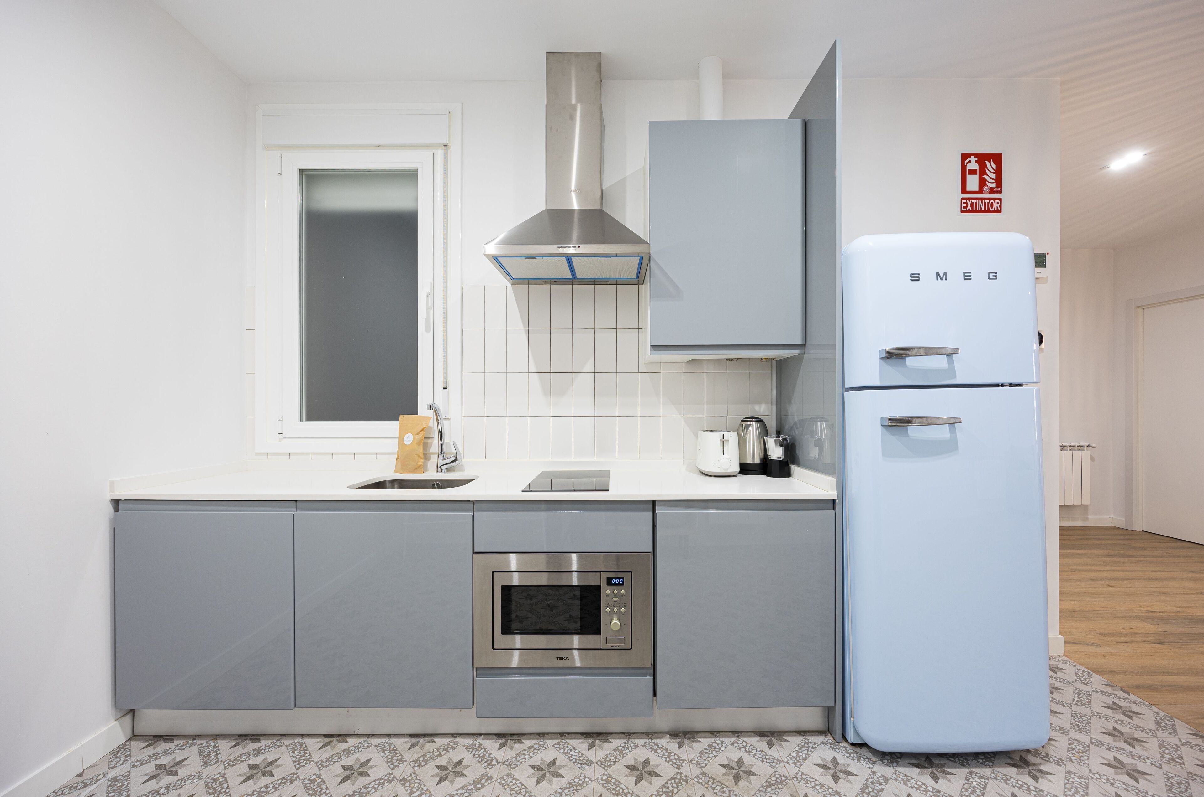 A modern kitchen with grey cabinets, a stainless steel range hood, a white refrigerator, and a built-in oven.