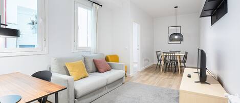 A modern living room with a grey sofa, wooden table, and a TV on a wooden stand.