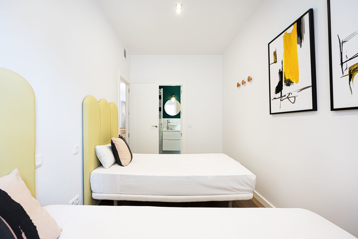 A bedroom with a bed, a bedside table, a mirror, and artwork on the wall.