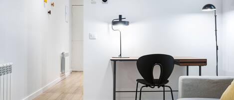 A modern, minimalist room with a wooden floor, a black chair, a grey sofa, and a desk with a lamp.
