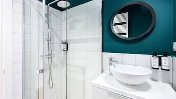 Un baño moderno con ducha de vidrio, lavamanos blanco y paredes color turquesa.