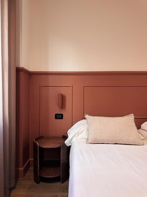 Une chambre d’hôtel comprenant un lit, une table de chevet, une petite table et un luminaire fixé au mur.