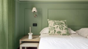 A room with a green wall, a bedside table with a lamp, a power outlet, and a decorative item. - Mercanzia apartment. (Bologna)