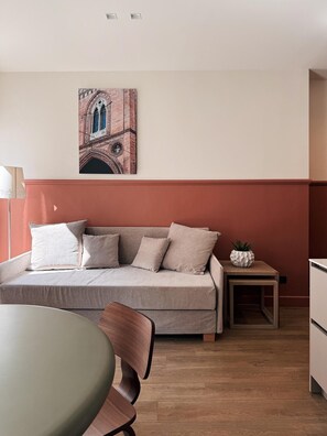 A modern living room with a sofa, a dining table, and a small side table with a plant.