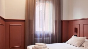 Une chambre d’hôtel avec deux lits, une fenêtre avec des rideaux légers et un plancher en bois.