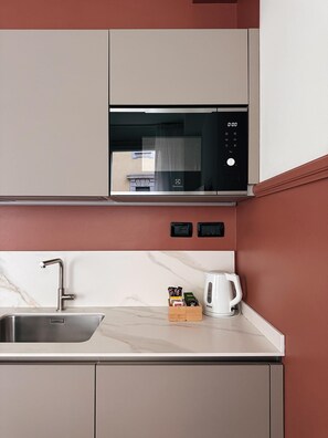 Una cocina con un lavamanos de acero inoxidable, un microondas y un hervidor sobre la encimera.