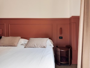 Een hotelkamer met een groot bed, twee kussens, een nachtkastje en een bijzettafeltje.