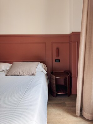 Une chambre d’hôtel avec un lit, une petite table d’appoint en bois et un panneau de commande fixé au mur.