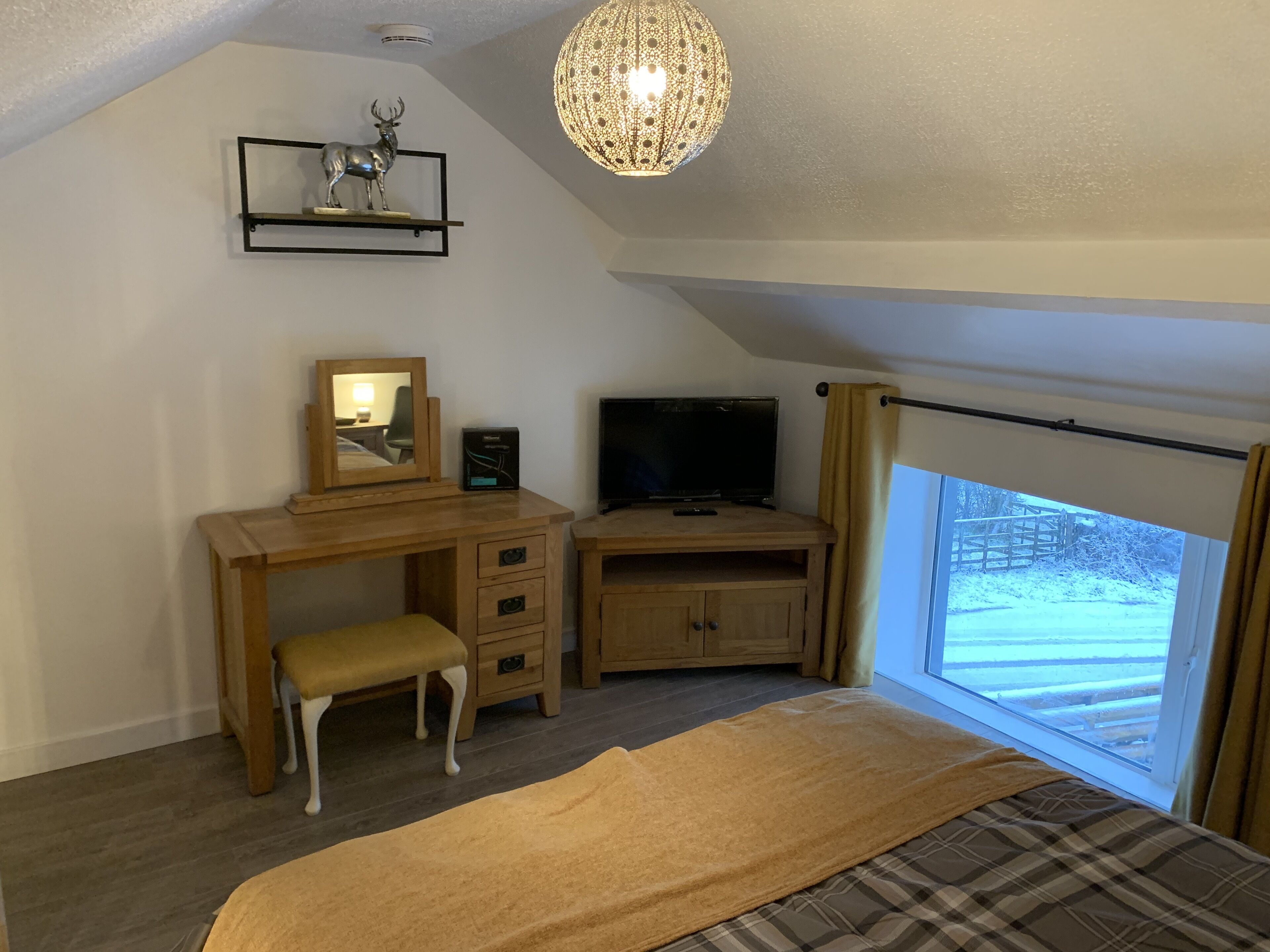 A bedroom with a bed, a desk, a television, a mirror, and a window with a view of a snowy landscape.
