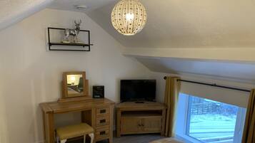 A bedroom with a bed, a desk, a television, a mirror, and a window with a view of a snowy landscape.