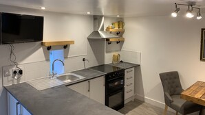 A compact kitchen with a built-in oven, a sink, and a wooden table. - Delightful One Bed Lake District Cottage (Penrith)