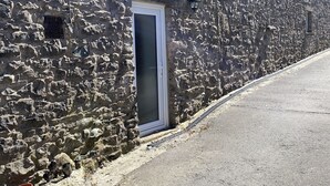 A stone building with a narrow entrance door, a small window, and a metal railing along the edge. - Delightful One Bed Lake District Cottage (Penrith)