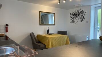 A dining area with a table covered in a yellow tablecloth, a chair, a mirror on the wall, and a decorative wall piece.