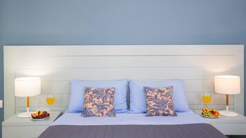 Una cama bien hecha con dos almohadas, una mesita de noche con frutero y un vaso de jugo de naranja, y una lámpara a cada lado de la cama.