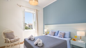 Ein Schlafzimmer mit einem Bett, einem Sessel, einem Nachttisch mit Lampe und einem Fenster.