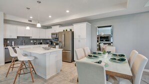 A modern kitchen with white cabinetry, a central island, and a dining area with a table set for four. - 2bd/2ba condo close to Disney, Gated community at Storey Lake (Kissimmee)