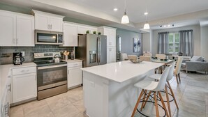 A modern kitchen with white cabinets, stainless steel appliances, and a central island with bar stools. - 2bd/2ba condo close to Disney, Gated community at Storey Lake (Kissimmee)