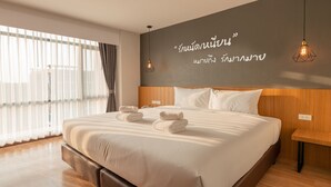 Une chambre d’hôtel moderne avec un grand lit, une tête de lit en bois et un mur orné d’inscriptions en thaï.