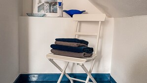 Una habitación de esquina con una silla plegable blanca, un cuenco azul en un estante y un cuadro en la pared.