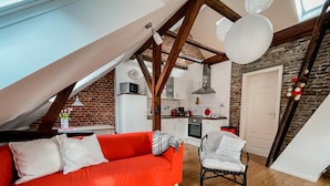 A cozy loft apartment with a red sofa, a dining area, a kitchen, and a staircase.