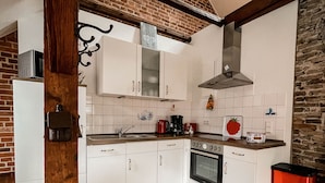 A kitchen with white cabinets, a brick wall, a wooden floor, and a red trash bin.