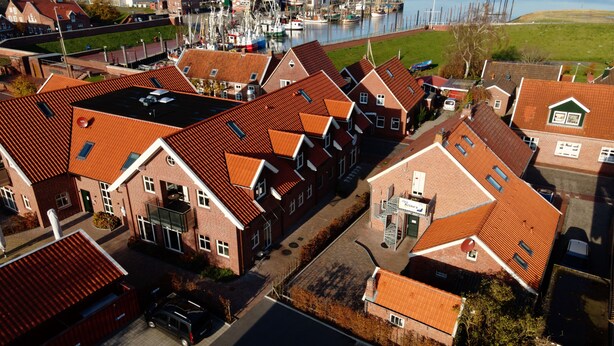 A residential area with red-tiled roofs, a marina with boats, and wind turbines in the background.