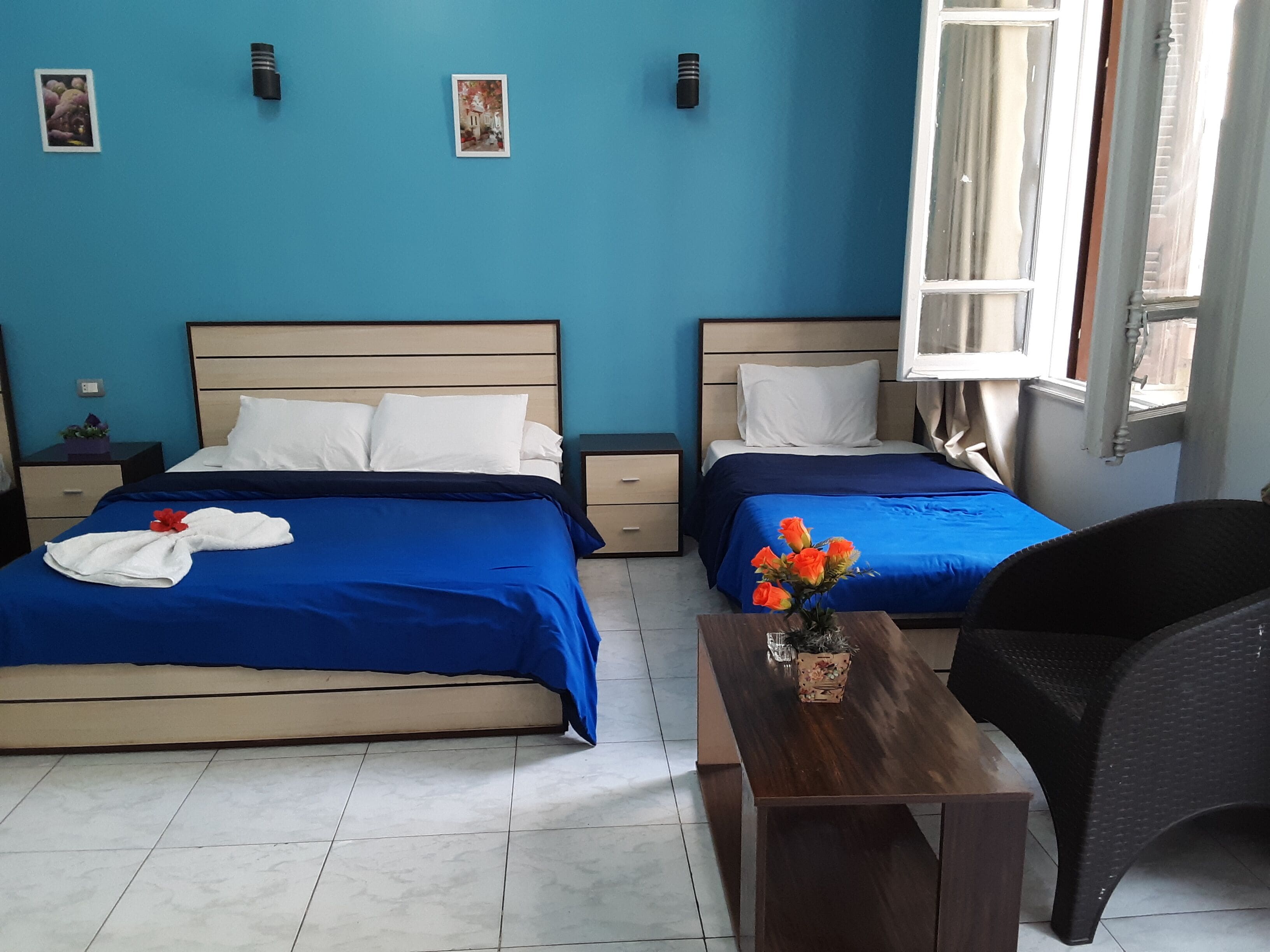 Une chambre d’hôtel avec deux lits, une petite table sur laquelle se trouve un vase, et une fenêtre avec des rideaux.