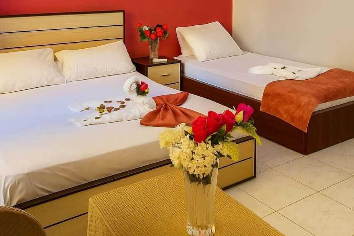 A hotel room with two beds, a wooden headboard, a small table with a vase of flowers, and wall-mounted lights.