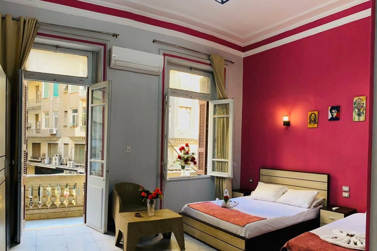 A hotel room with a bed, a small table with flowers, a chair, and a view of the outside balcony.