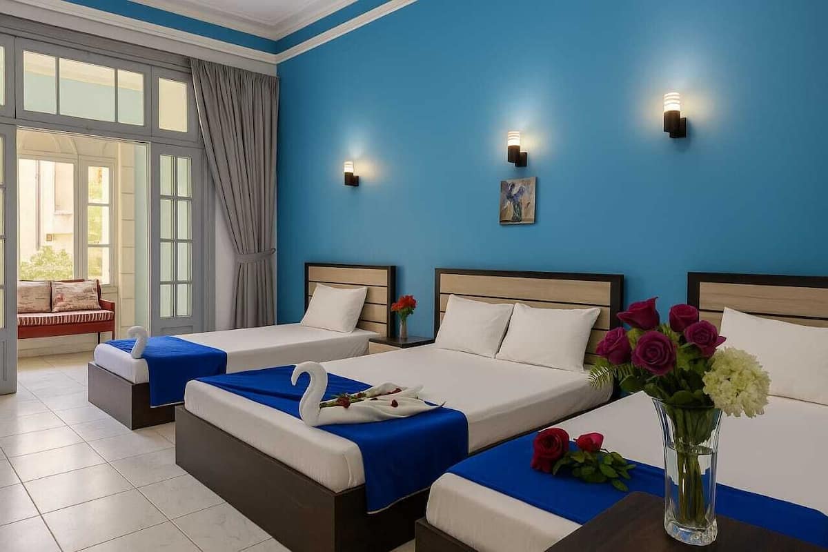 A hotel room with two beds, a sitting area with a sofa, and a large window with curtains.