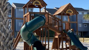 A wooden playground with slides and climbing structures, set against a backdrop of residential buildings. - Gated resort on CSB.End unit w/easy walk to beach. Beach cart & chairs included. (Port St Joe)