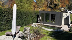 Ein moderner Außenbereich mit einer Holterrasse, einem weißen Sonnenschirm und einem kleinen, holzverkleideten Bauwerk mit einer Leiter.