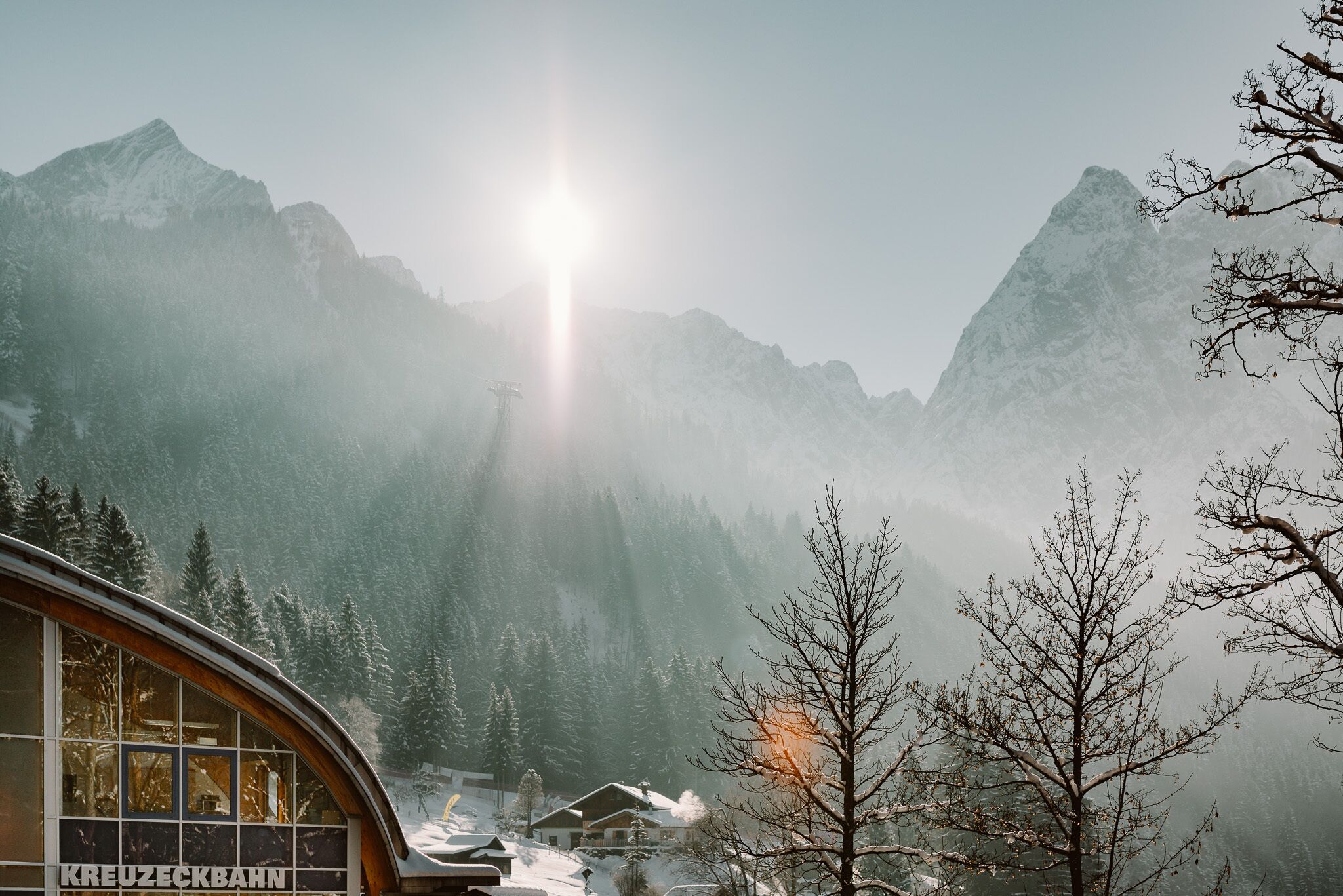 A mountain cabin with a view of snow-covered peaks and a forested valley.