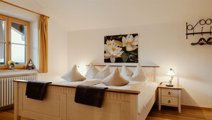 Ein Schlafzimmer mit einem hölzernen Bett, weißer Bettwäsche, einem Nachttisch mit Lampe, einem Fenster mit Vorhängen und einem wandmontierten Regal.