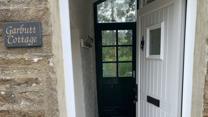 En hvedeblok med en stenvæg, et skilt med teksten "Garbutt Cottage", en hvid dør og et lille vindue.