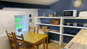 Et kompakt køkken med et træbord og stole, en mikroovn, en komfur og reoler med køkkenudstyr.