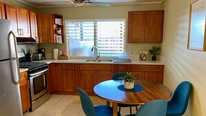 A kitchen with wooden cabinets, a stainless steel refrigerator, a stove, and a dining table with blue chairs. - Diamond Head/Waikiki Surf Shack 2-Bedroom Private Ohana Unit (Honolulu)