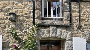 Un edificio in pietra con una porta di legno, una finestra con un fiore e un lampadario in metallo.
