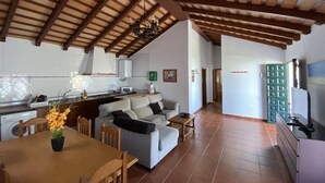 A spacious living area with a high ceiling and exposed wooden beams, a kitchen with modern appliances, and a dining area with a table and chairs. - Villas Atlantico Sur (Conil de la Frontera)